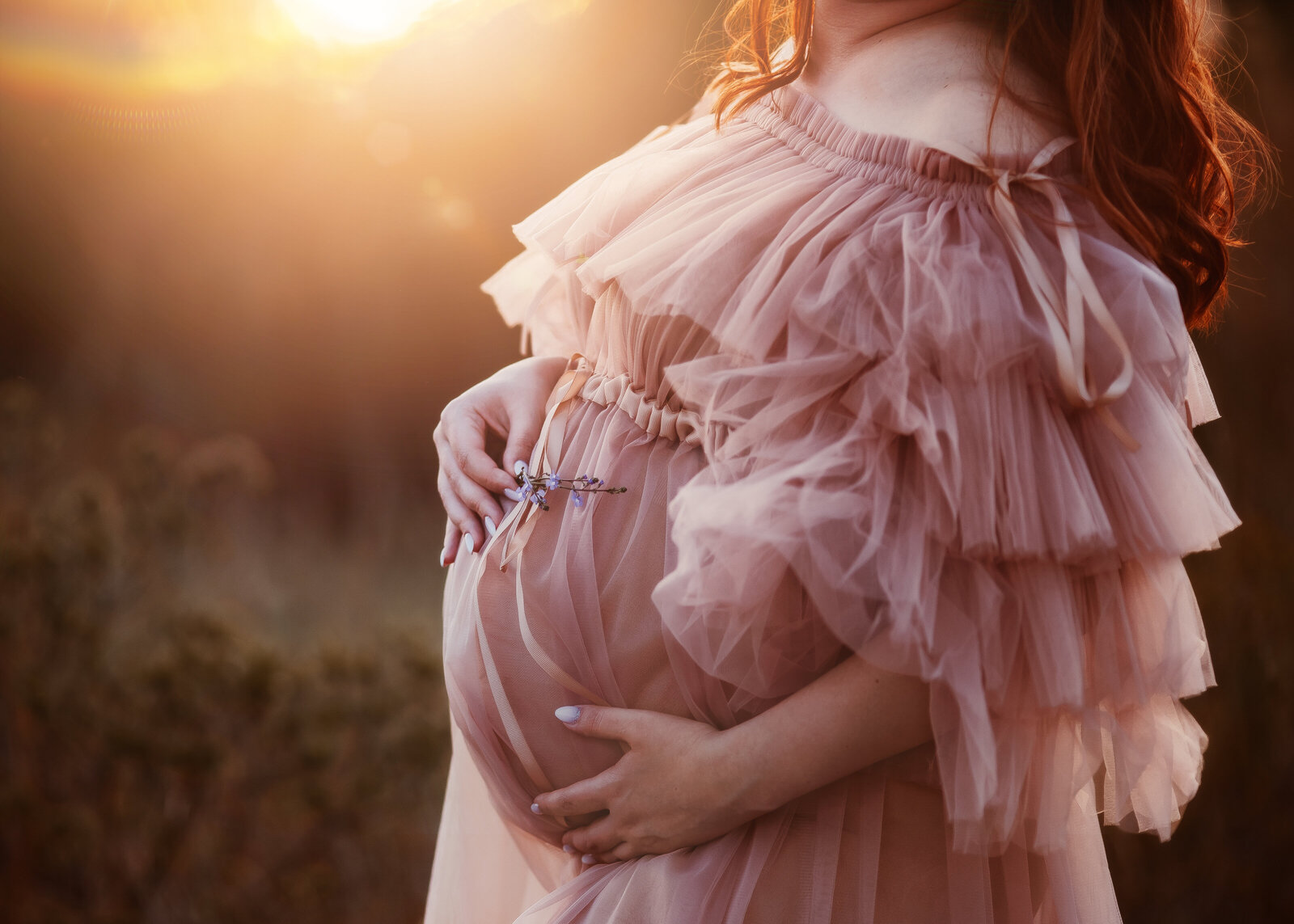a close up of a pregnant belly woman hugging it while holding a flower on top of it and there is a beautiful golden sunset light in the background